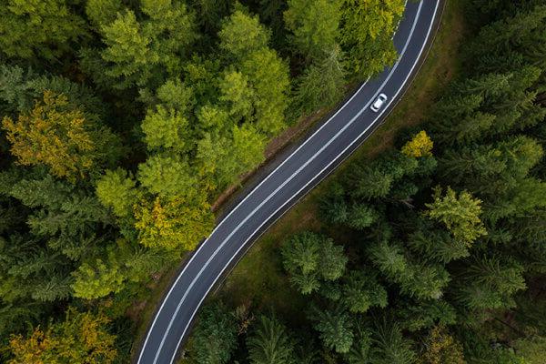 Bird's eye view of a car driving on a bendy road through a surrounding green forest of trees